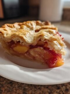 A slice of decadent brown butter strawberry peach pie on a white plate, showing flaky crust and juicy fruit filling.