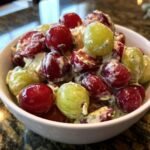 Close-up of Irresistible Chicken Salad Chick Grape Salad in a white bowl, featuring red and green grapes coated in creamy dressing.