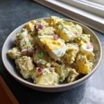 A bowl of Creamy Potato Salad With Egg, garnished with fresh dill and red onion, perfect for a picnic.