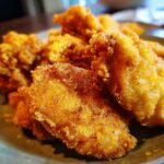 Close-up of golden brown, crispy cornmeal fried fish pieces piled on a plate.