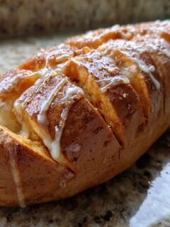 A close-up of a loaf of Delicious Baked Sweet Potatoes With Cinnamon Honey, drizzled with a sweet glaze.