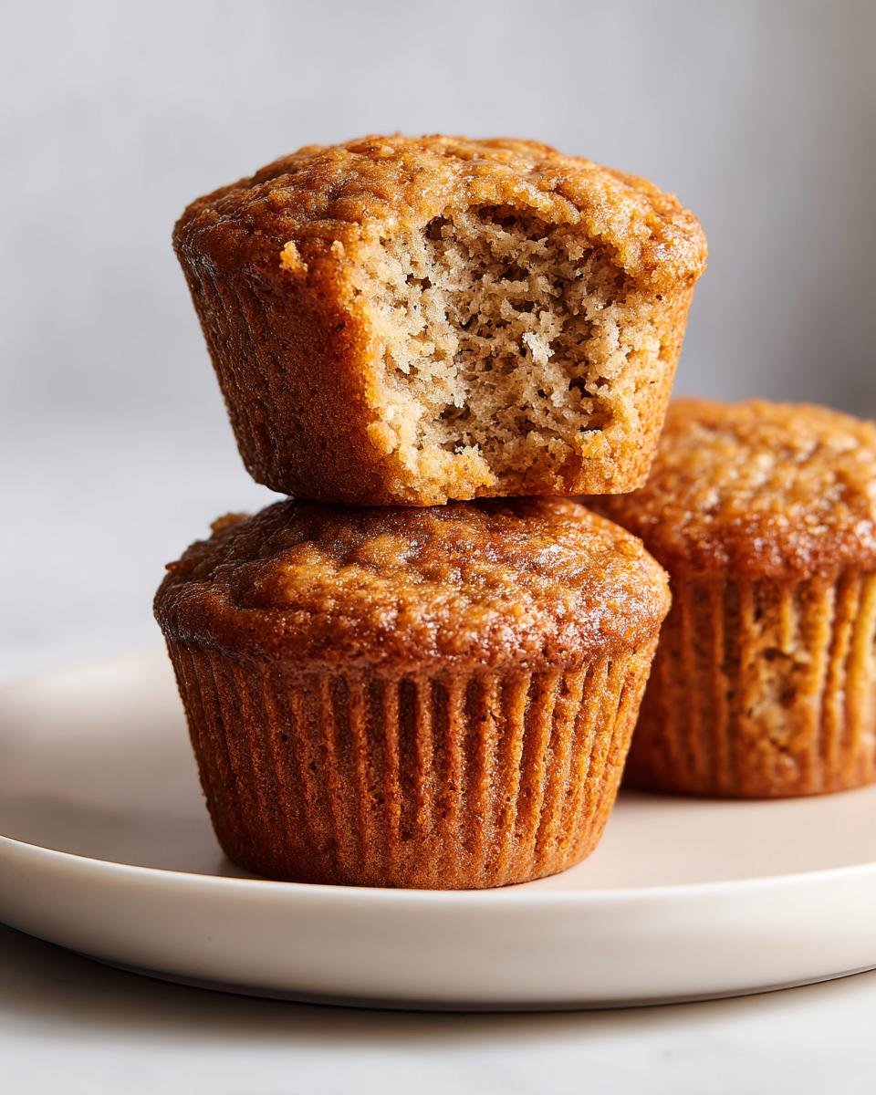A stack of three Delightful Fathers Day Banana Muffins, with the top one having a bite taken out, revealing the moist interior.
