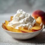A bowl of sliced peaches topped with a generous dollop of whipped cream, a delightful peaches and cream summer treat.
