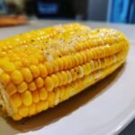 Two ears of perfectly cooked Easy Microwave Corn On The Cob, glistening with butter and sprinkled with black pepper.
