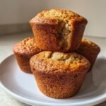 A stack of three Delightful Fathers Day Banana Muffins on a white plate, with one muffin having a bite taken out.
