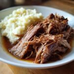 A close-up of tender, shredded crock pot roast served with creamy mashed potatoes, perfect for Father's Day.