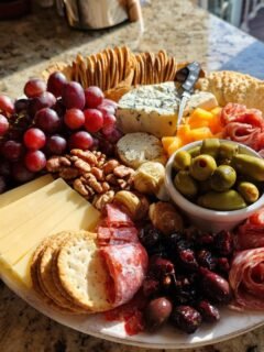 A Fathers Day snack plate featuring grapes, cheese, crackers, olives, salami, and dried fruit.