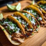 Close-up of delicious Flavorful BBQ Chicken Tacos Sweet And Smoky topped with onions and cilantro, served with lime wedges.