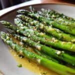 Close-up of tender, bright green roasted asparagus spears coated in a glistening lemon garlic butter sauce with herbs.