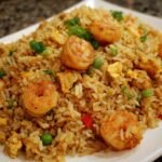 A close-up of flavorful shrimp fried rice, featuring plump shrimp, scrambled eggs, peas, and green onions.