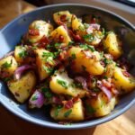 Close-up of a bowl filled with Flavorful Warm German Potato Salad, featuring chunks of potatoes, red onion, crispy bacon, and fresh parsley.