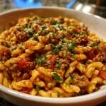 A close-up of a bowl of pasta with ground beef and tomato sauce, garnished with parsley.