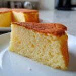 A slice of fluffy and light Heavenly Japanese Cheesecake on a white plate, with the rest of the cake blurred in the background.