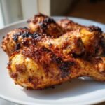 Close-up of Irresistible Baked Chicken Drumsticks Crispy Delight on a white plate, showing golden-brown, crispy skin.