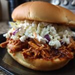 A close-up of an irresistible BBQ chicken sandwich piled high with shredded chicken and creamy coleslaw on a bun.