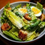 Close-up of a bowl filled with an Irresistible Caesar Salad Recipe, featuring crisp romaine lettuce, croutons, and halved boiled eggs.