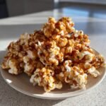 A pile of Irresistible Caramel Popcorn Balls glistening with caramel on a light-colored plate.
