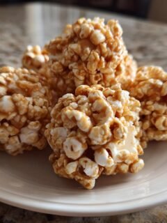A close-up of several Irresistible Caramel Popcorn Balls piled on a white plate, glistening with caramel.
