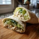 A delicious Irresistible Chicken Caesar Wrap cut in half, showcasing shredded chicken, crisp lettuce, and creamy Caesar dressing.