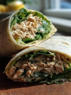 A close-up of an Irresistible Chicken Caesar Wrap cut in half, showcasing shredded chicken, crisp lettuce, and creamy dressing.
