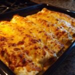 Close-up of Irresistible Chicken Enchiladas With Sour Cream Sauce baked in a dish with melted golden cheese.