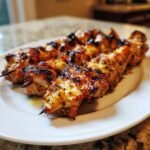 Close-up of perfectly grilled, irresistible chicken skewers on a white plate, showcasing golden-brown char marks.
