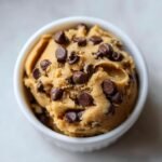 A close-up view of a white bowl filled with irresistible edible cookie dough loaded with chocolate chips.