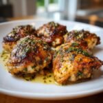 A plate of five Irresistible Garlic Herb Roasted Chicken Thighs, glistening with sauce and herbs.
