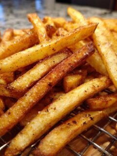 A close-up of a pile of Irresistible Homemade French Fries, perfectly golden and seasoned on a wire rack.