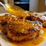A spoon is drizzling a golden honey butter garlic sauce over perfectly cooked pork chops.