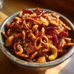 A close-up of a bowl filled with Irresistible Hot Honey Chex Mix, featuring pretzels, nuts, and Chex cereal coated in a glossy glaze.