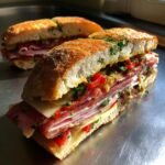Close-up of an Irresistible Italian Sandwich packed with layers of deli meats, cheese, and peppers.