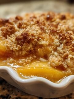 Close-up of an Irresistible Peach Crisp With Fresh Peaches in a white ramekin, showing juicy peaches and a crumbly topping.