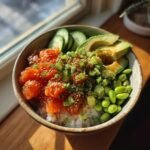 A close-up of an irresistible sushi bowl featuring rice, marinated salmon, avocado, edamame, and cucumber slices.