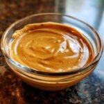 Close-up of Irresistible Thai Peanut Sauce in a clear glass bowl, showing its creamy texture.