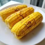 Three ears of perfectly cooked air fryer corn on the cob, lightly charred and glistening, served on a white plate.