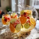 A pitcher and glasses filled with Refreshing White Sangria Recipe For Summer Bliss, packed with strawberries, oranges, and limes.