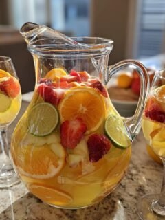 A pitcher and glass filled with Refreshing White Sangria Recipe For Summer Bliss, packed with fresh fruit like oranges, strawberries, and limes.