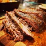 Close-up of tender, sliced Savory Traeger Mississippi Pot Roast on a wooden cutting board, glistening with juices.
