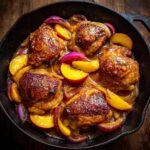 A cast iron skillet filled with Sweet Savory Peach Chicken, sliced peaches, and red onions in a glossy sauce.
