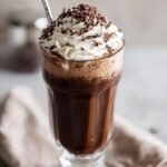 A tall glass filled with a rich chocolate milkshake, topped with whipped cream and chocolate shavings. Indulge In The Ultimate Chocolate Milkshake Delight.