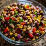 A vibrant bowl of Ultimate Cowboy Caviar, a colorful party appetizer with beans, corn, peppers, and onions.