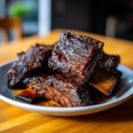 A plate piled high with glistening Ultimate Smoked Beef Short Ribs, showcasing their rich, dark, and tender texture.