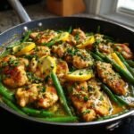 Close-up of Zesty Lemon Garlic Butter Chicken and Green Beans cooked in a skillet, garnished with lemon slices and parsley.