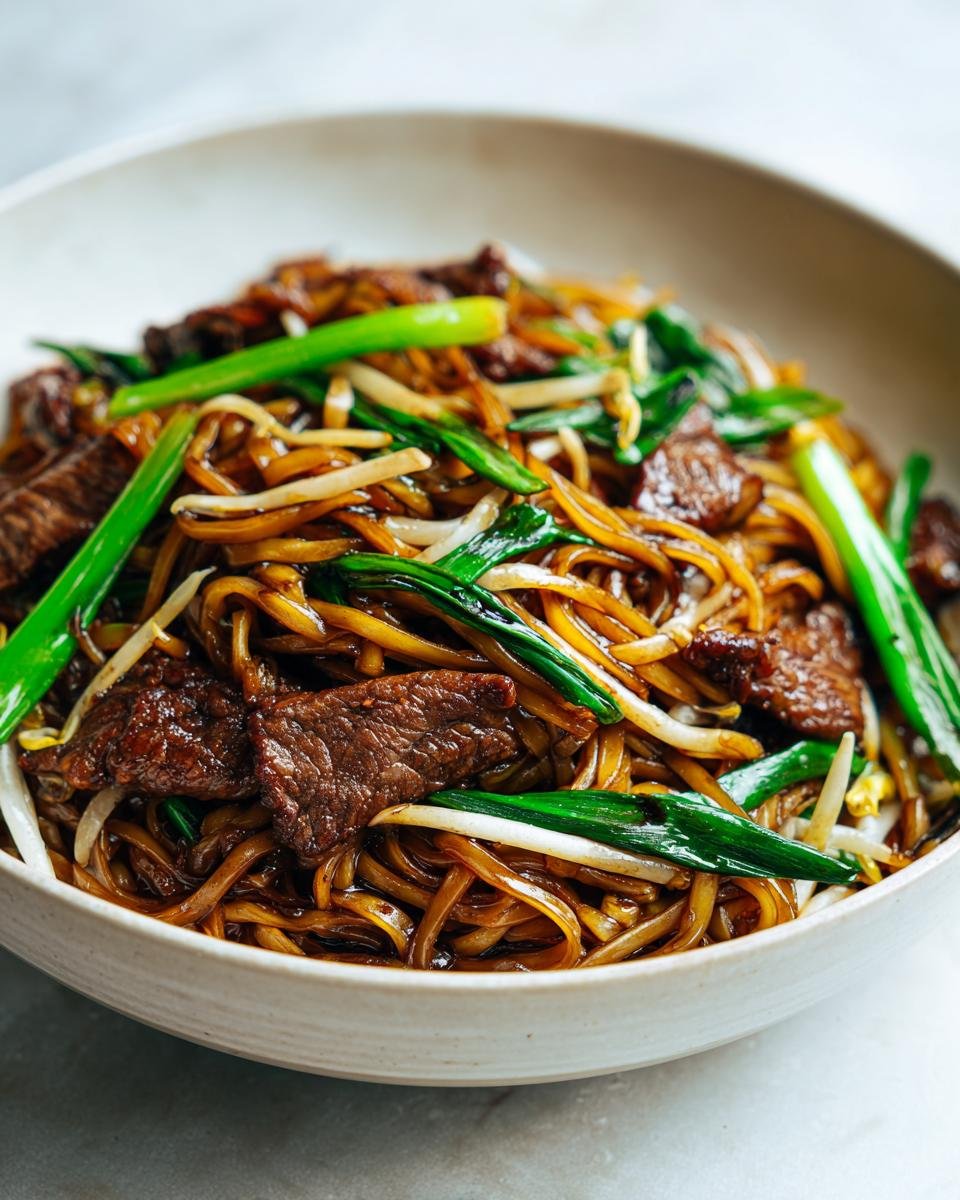 A close-up serving of glossy Beef Chow Fun noodles mixed with sliced beef, bean sprouts, and bright green scallions.