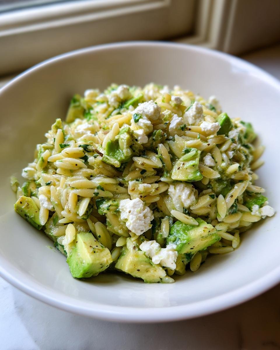 A close-up of a serving of Avocado Feta Orzo Salad featuring orzo pasta, bright green avocado chunks, and crumbled white feta cheese.