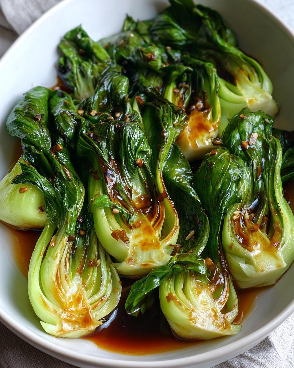 Close-up of tender, glossy Baby Bok Choy halves covered in a dark, savory sauce and sesame seeds.