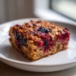 A single, golden-brown square of Berry Baked Oatmeal topped with baked, juicy red and dark berries.