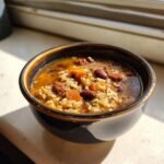 A close-up of a dark bowl filled with Chorizo Rice Bean Soup, showing rice, red beans, and orange vegetables.