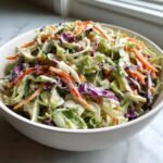 A close-up of a white bowl filled with fresh, creamy Coleslaw featuring shredded green cabbage, red cabbage, and carrots.